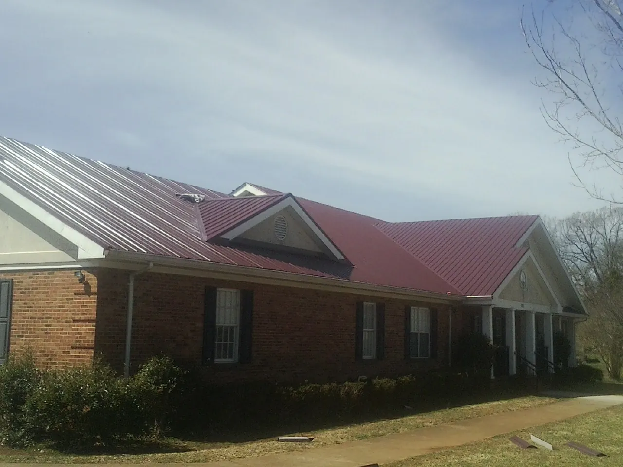 Red metal roof with gabled entries on a long brick building, from a Hail Damage Roof Repair job in Darlington