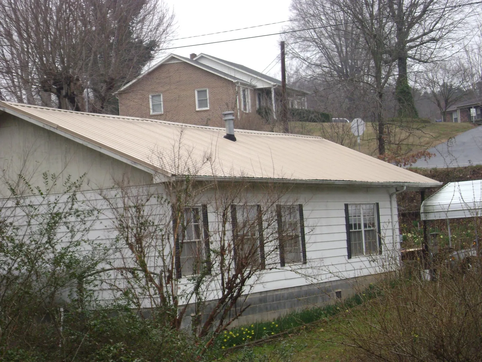 Tan metal roof on a white sided house set into a hillside — Commercial Roofing by Roofing Brothers in Darlington